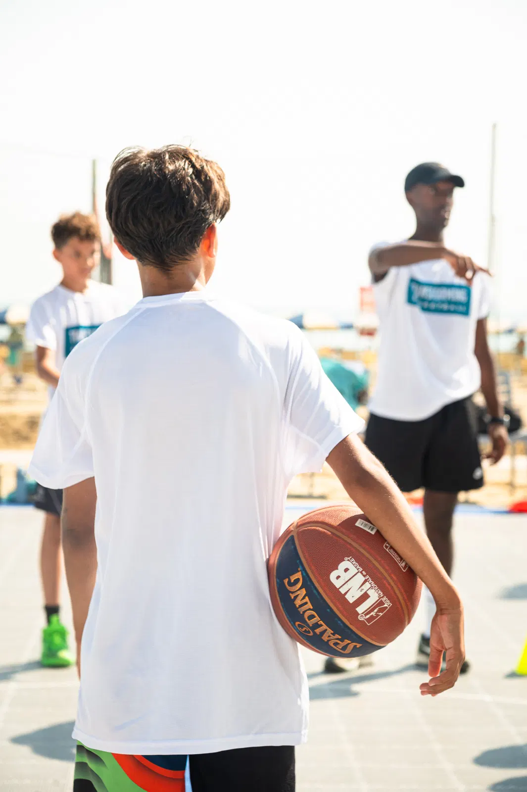 A coach pointing out a cue to a player holding a basketball at an outdoor camp