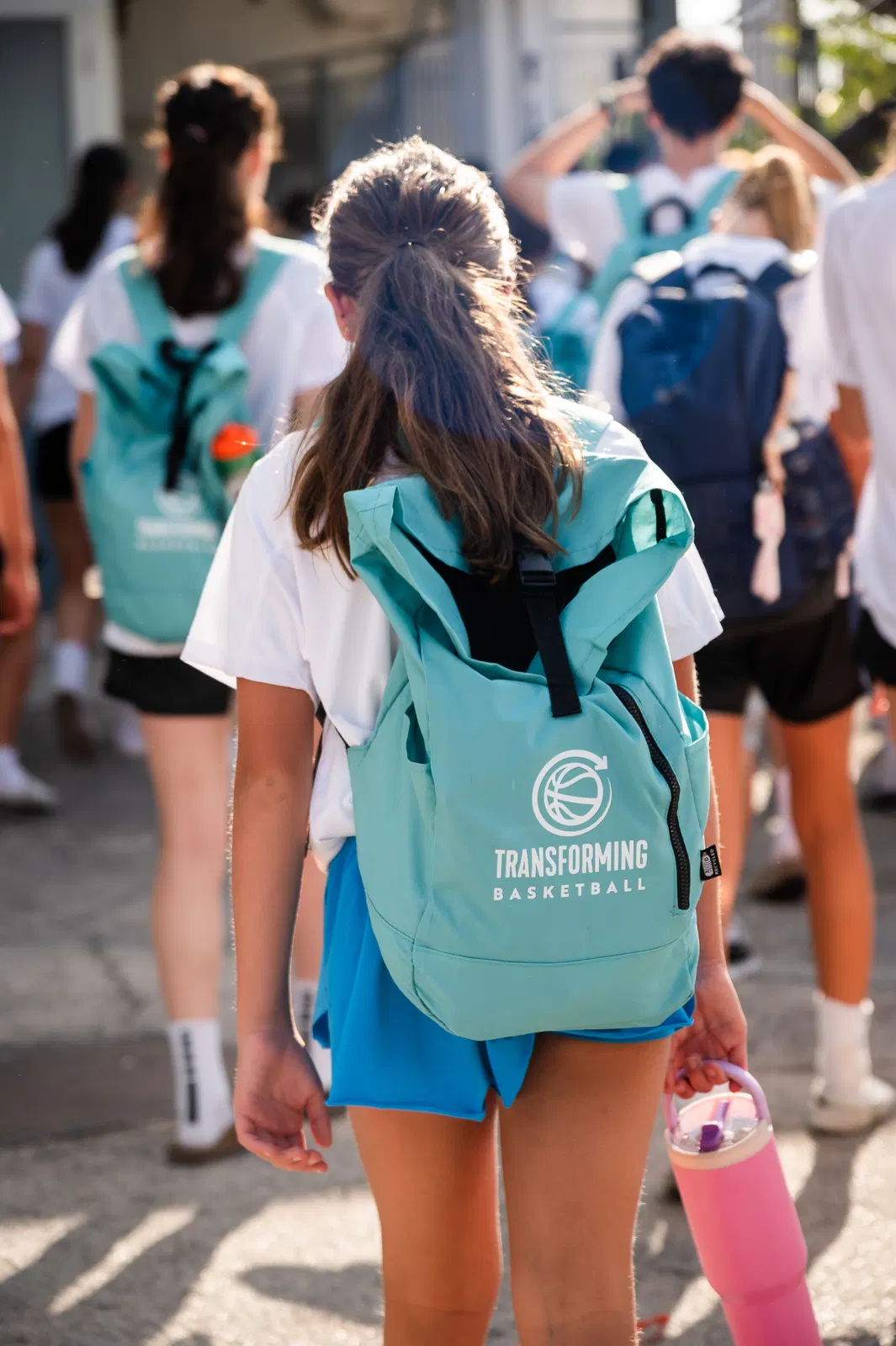 A young player carrying a teal Transforming Basketball backpack walking to the court