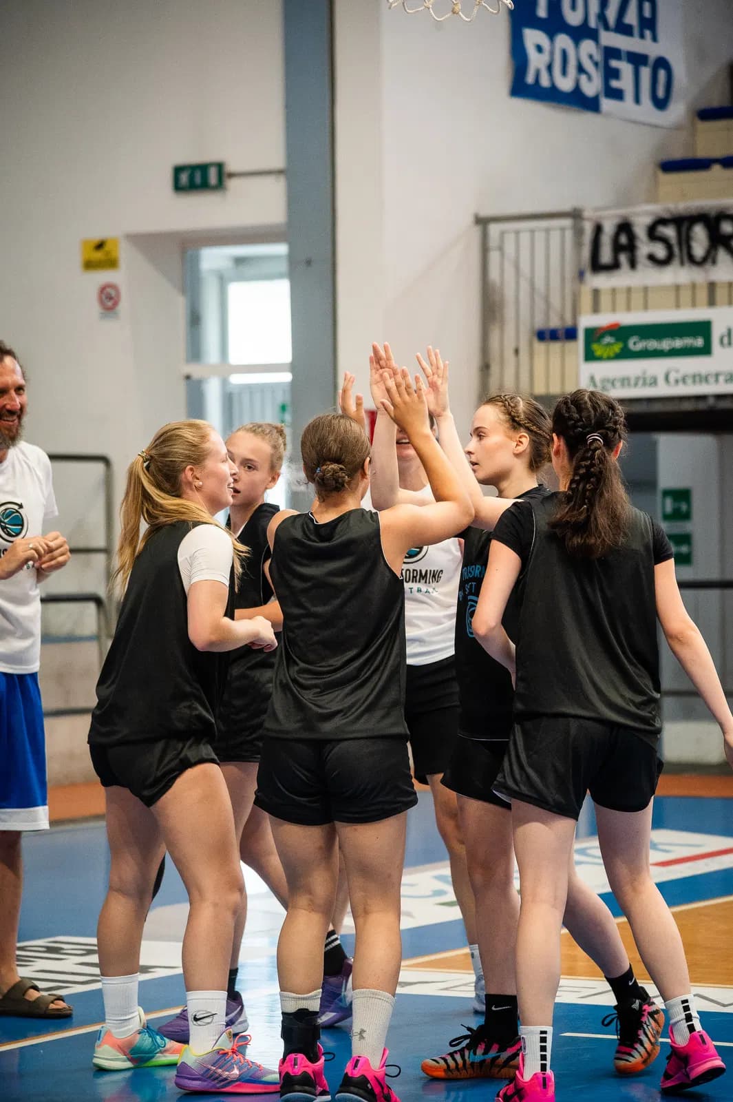 A team in Transforming Basketball pinnies high-fiving in a huddle with their coach
