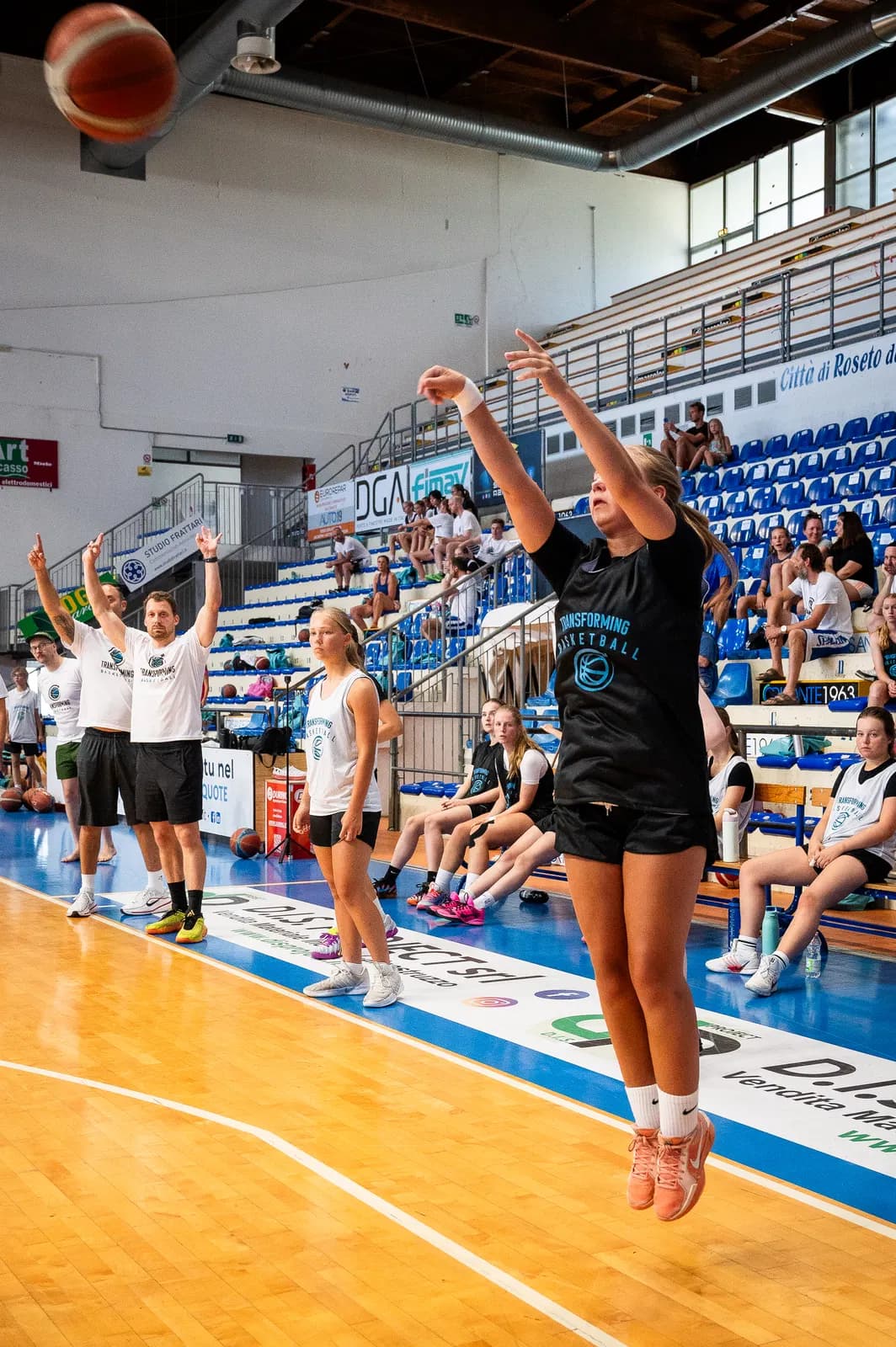 A player shooting at one basket while coaches and teammates watch