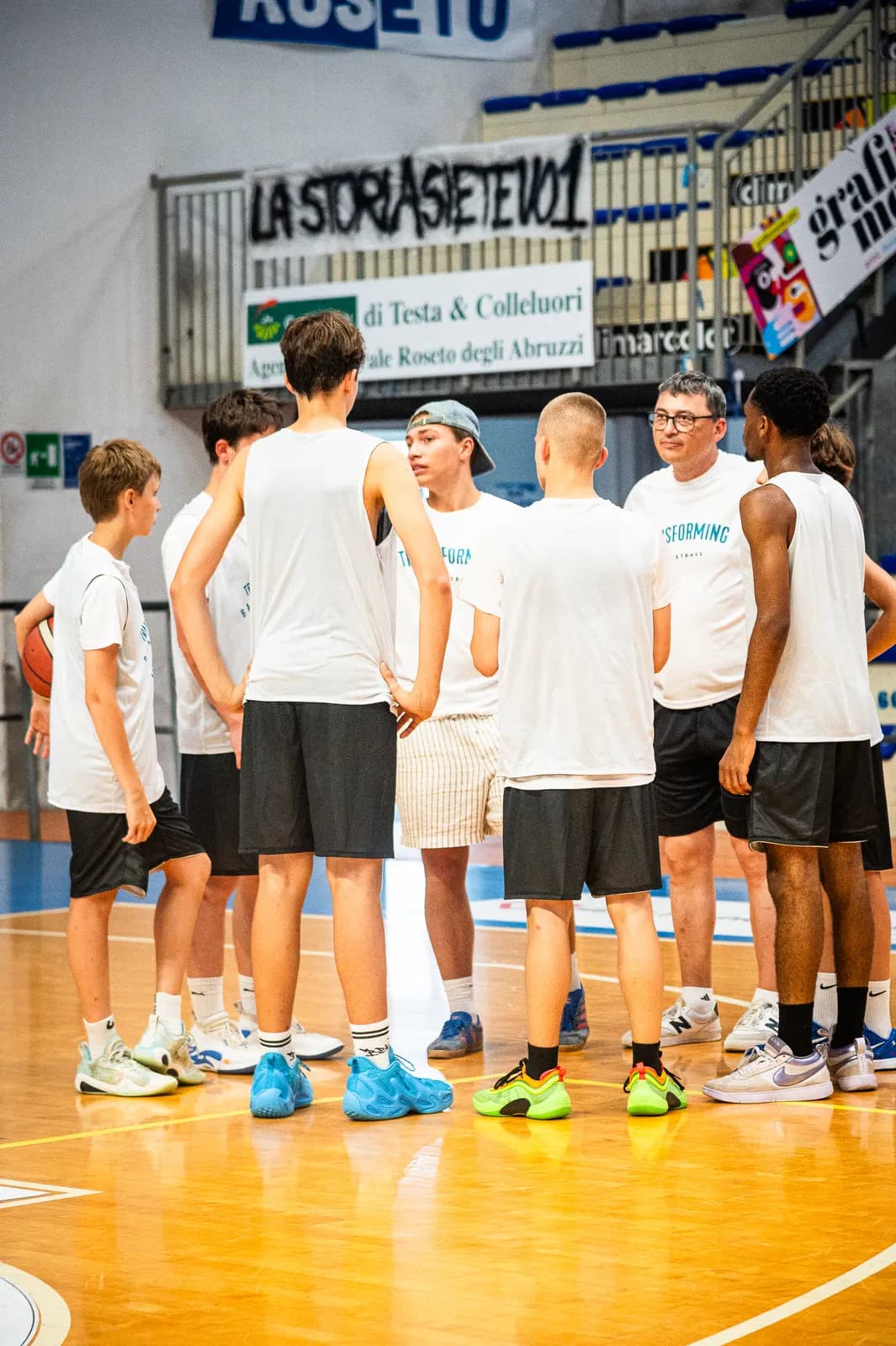 A coach talking with a group of players between activities at the 2026 Transforming Basketball camp in Roseto