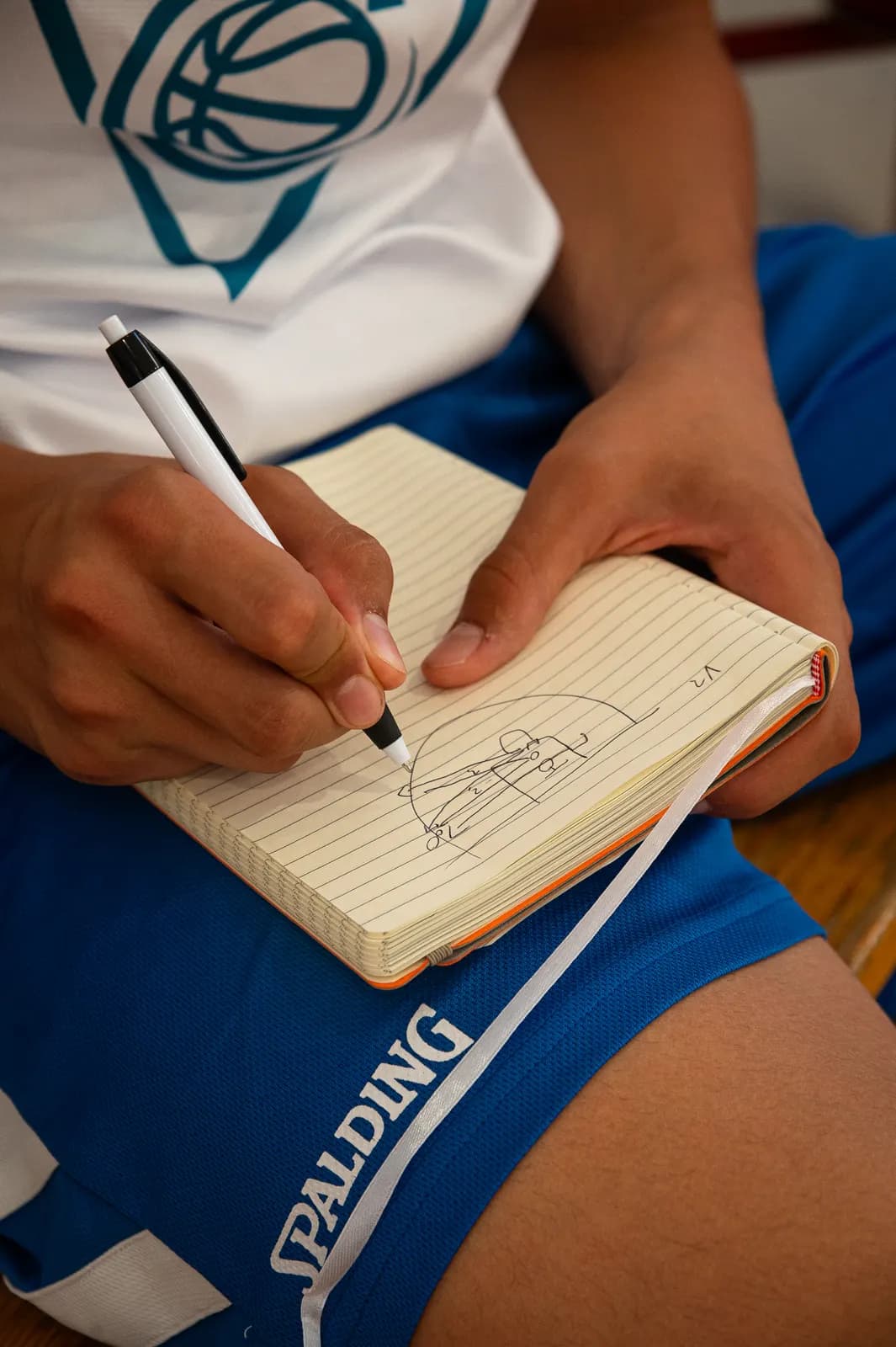 Sketching a play diagram in a notebook during a Transforming Basketball camp session in Roseto