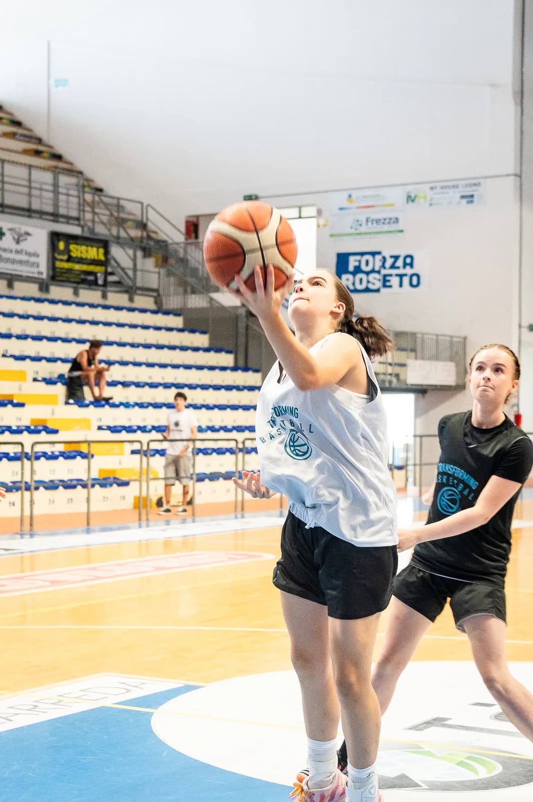 A player rising for a layup as a defender chases from behind during a game at the 2026 Transforming Basketball camp in Roseto