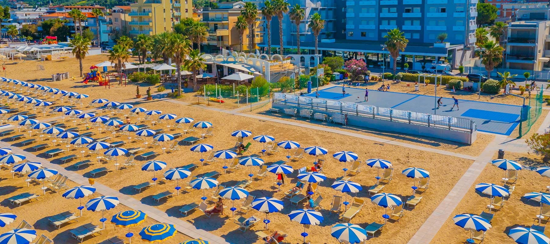 Beachfront basketball court beside rows of blue-and-white parasols on the sand at Roseto degli Abruzzi